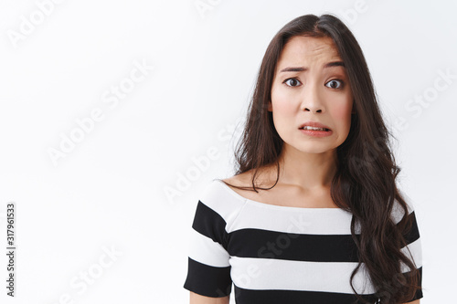 Embarrassed and confused insecure young asian female made mistake, feel sorry or pity, cringe nervously, clench teeth and pulling sad worried face, frowning panicking, standing white background photo