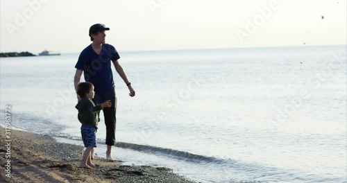 Father and toddler son throwing rocks into ocean at sunset - wide shot photo