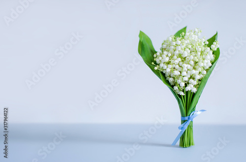 A bouquet of lilies of the valley tied with a blue ribbon on a blue background. Copy space