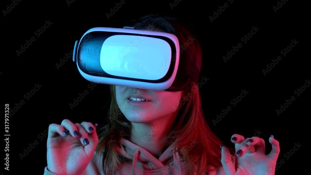 Young woman in VR glasses closeup. A woman immersed in virtual reality makes movements with her hands. Blue and red light falls on a woman on a black background.