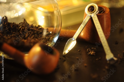 Tools for cleaning smoking pipes, round glass vase with tabacco, smoking pipes and bokeh in the background