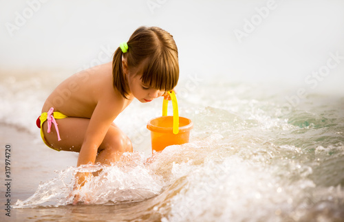 Wallpaper Mural Small girl in bright swimwear playing with toys in sea water edge on summer day
