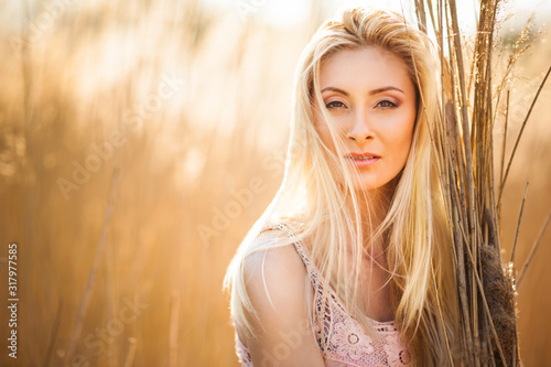 Portrait of young beautiful blonde smiling woman in yellow grass looking aside on clear sunny day. Woman natural beauty and summer nature concept