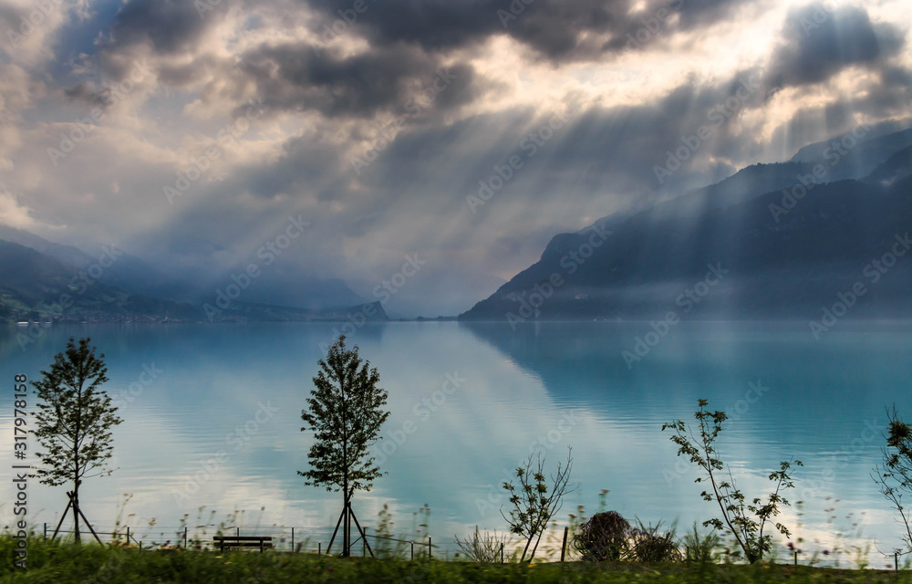 Fototapeta premium Beautiful blue lake and houses with the brown roofs in Alps in Switzerland are in the sunlight