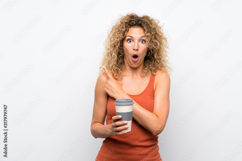 Young blonde woman with curly hair holding a take away coffee surprised and pointing side Young blonde woman with curly hair holding a take away coffee surprised and pointing side