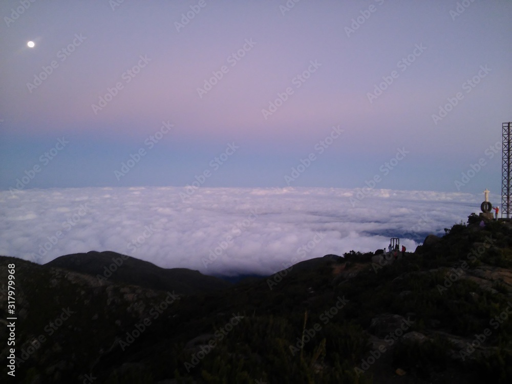 a sea of clouds and the moon up in the sky, in a dawning at Pico da Bandeira, BRazil, the third highest point of the country