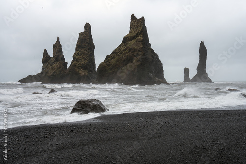 Waves crashing in on shore on Reynisfjara beach and black volcanic sand in Iceland. Basalt sculpture columns raises up from the sea in the background. Traveling and nature concept.