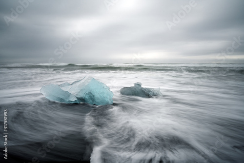 Crystal clear and blue ice chunks washes up on the black lava sand by the waves on diamond beach in Jokulsarlon glacier lagoon. Long exposure shot. © Jon Anders Wiken