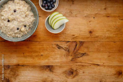 A bowl of nutritious blueberry and apple porridge and a small bowl of blueberries and apple, on a wooden background, withcopy space photo