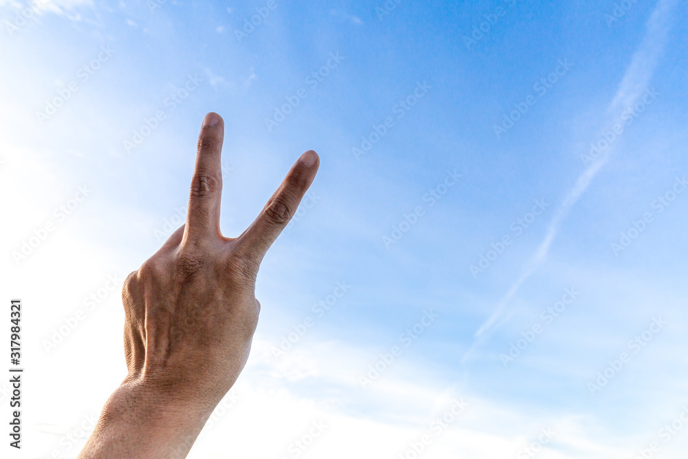 Man's hand showing two fingers up on sky Man's hand showing two fingers up on sky