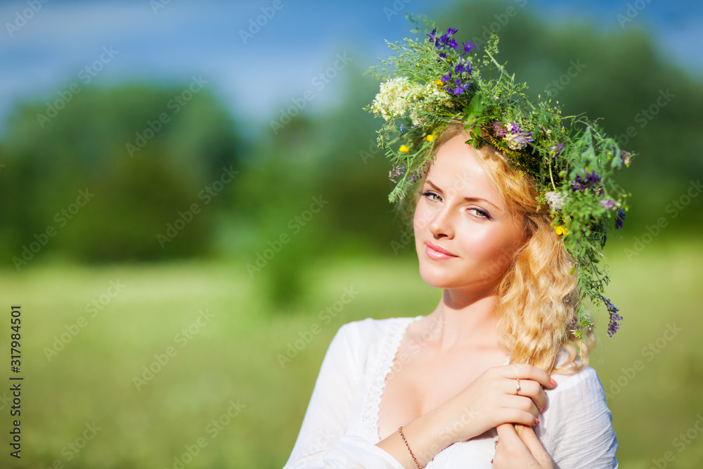 Young beautiful blond woman in white dress and floral wreath standing and looking at camera on summer day Young beautiful blond woman in white dress and floral wreath standing and looking at camera on summer day