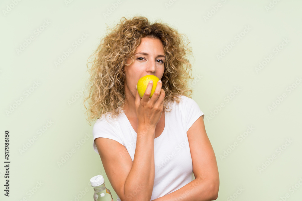 Young blonde woman with curly hair with an apple and with a bottle of water Young blonde woman with curly hair with an apple and with a bottle of water