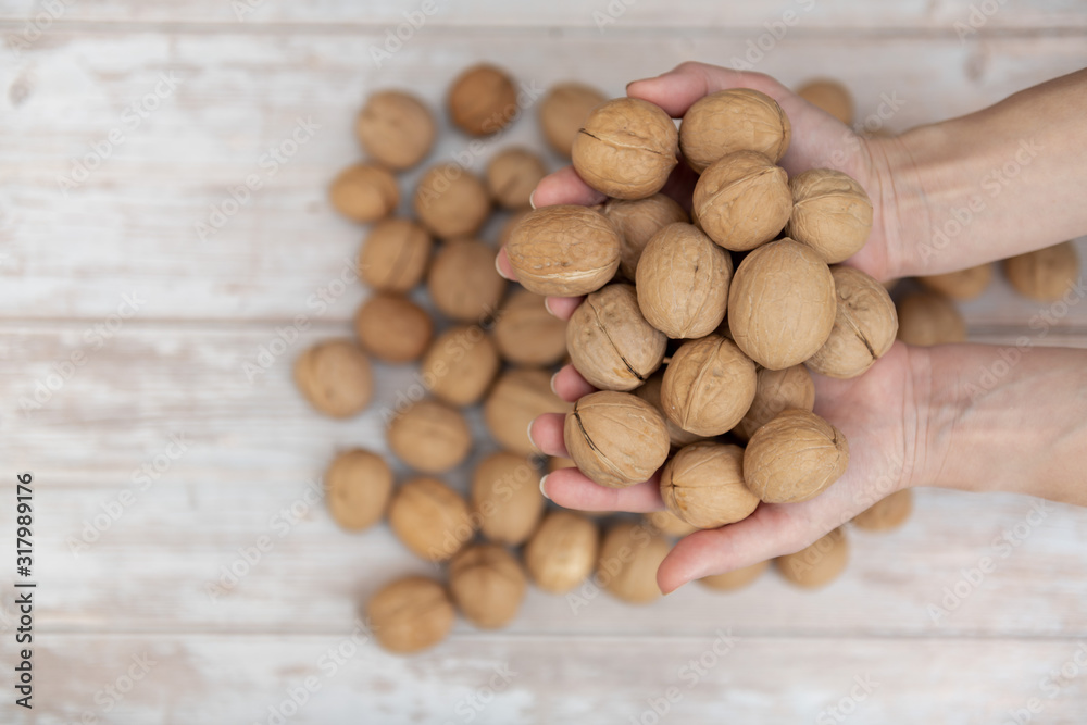 Obraz premium Hands holding whole walnuts on rustic old wooden table