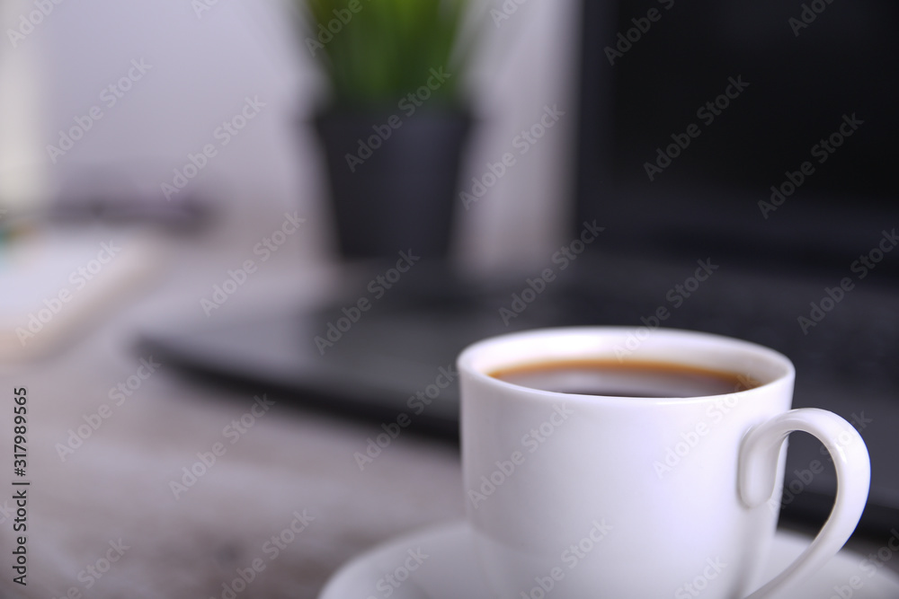 Obraz premium Cup of coffee on office desktop with laptop, computer on wooden table. Close up, with space for your text