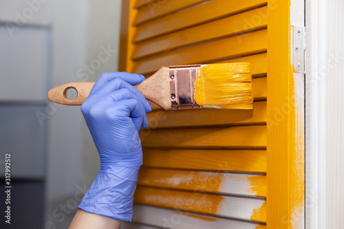 Closeup female hand in purple rubber glove with paintbrush painting natural wooden door with orange paint. Concept colored bright creative design interior for young family. How to Paint Wooden Surface