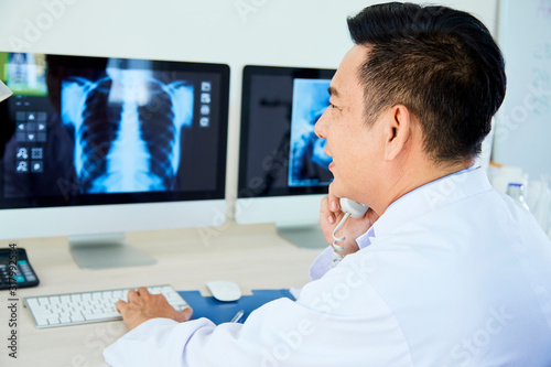 Professional pulmonologist giving call to his colleague to ask for advice while looking to X-ray images photo