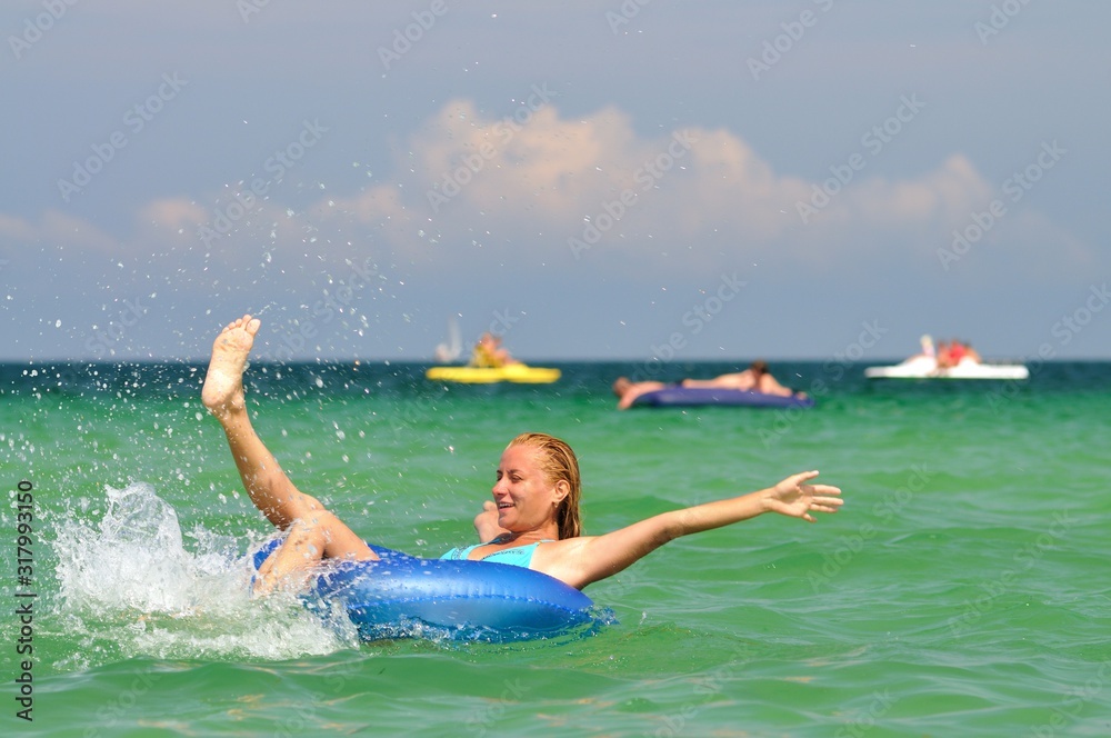 Young blond woman in blue bikini riding on swimming circle in sea and smiling