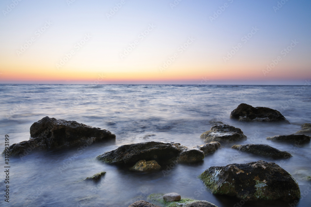 Beautiful pink sunset over still sea waters and water stones with green moss in Crimea