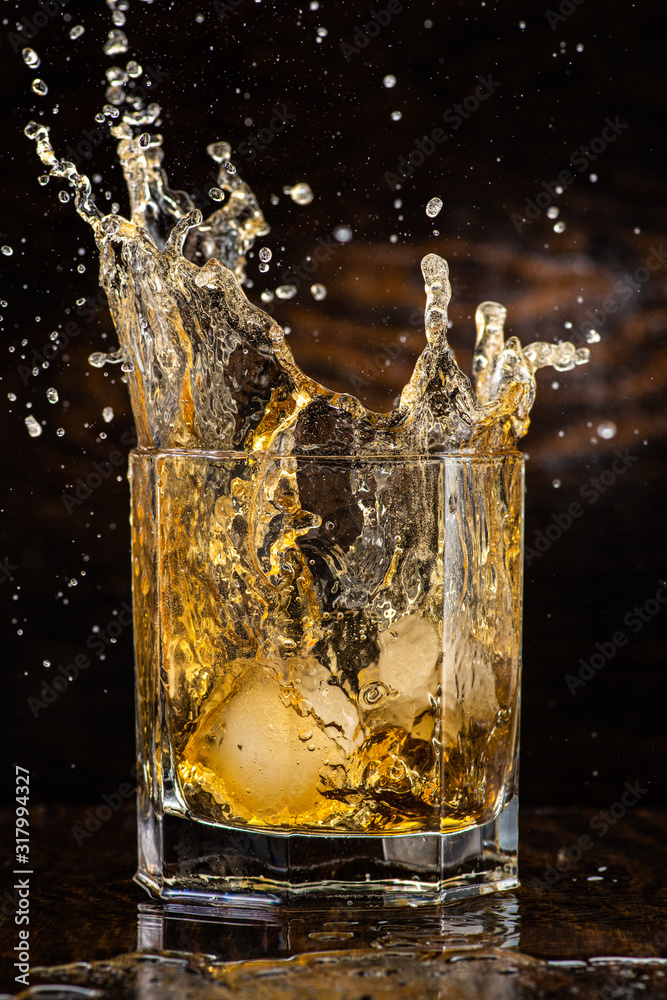 big splash in a glass with whiskey with ice on a dark wooden background big splash in a glass with whiskey with ice on a dark wooden background
