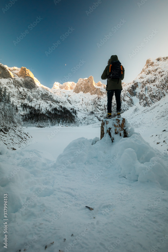 Man with backpack trekking in mountains. Cold weather, snow on Peaks