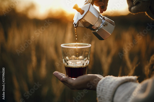 Canvas Traveler pouring fresh hot coffee from geyser coffee maker into glass cup in sunny warm light in rural countryside herbs