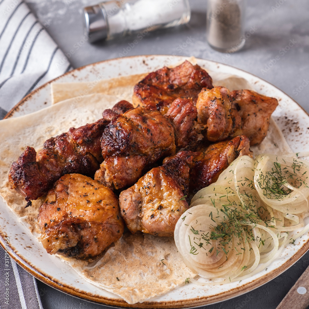 Pork shish kebab with onion and red sauce. Grilled meat. Barbecue pork meat on a plate