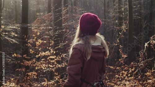 Young woman enjoying warm sun rays in autumn golden forest. Looking around and smiling feeling the weather.