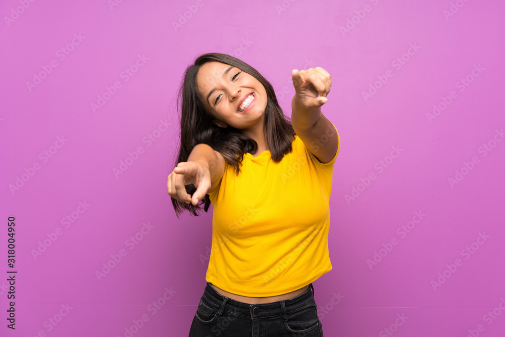 Young brunette girl over isolated background points finger at you while smiling - obrazy, fototapety, plakaty 