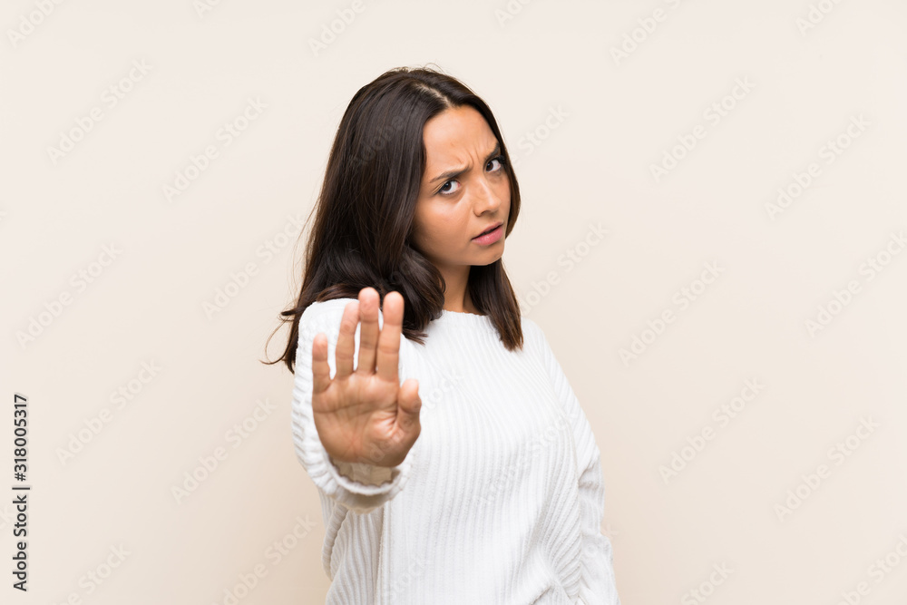 Young brunette woman with white sweater over isolated background making stop gesture with her hand Young brunette woman with white sweater over isolated background making stop gesture with her hand