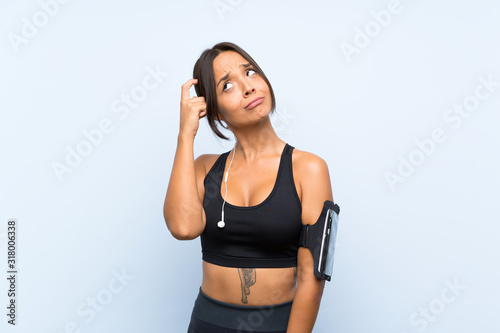 Young sport girl over isolated blue background having doubts and with confuse face expression