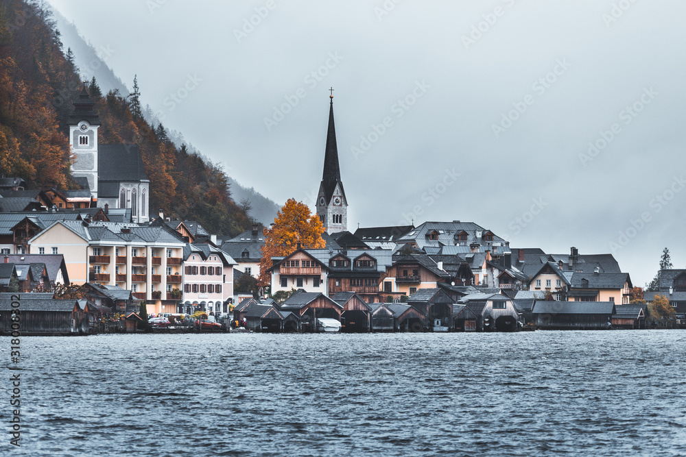 Moody fall scenery of Hallstatt at dawn, a peaceful lakeside village & a UNESCO heritage site in Salzkammergut region of Austria, with fog around and majestic mountains in background