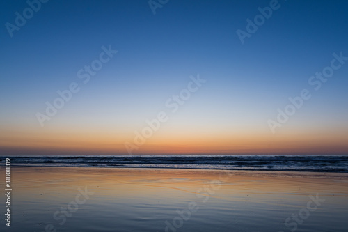 Sunset over the sea reflected in the wet sand of a beach