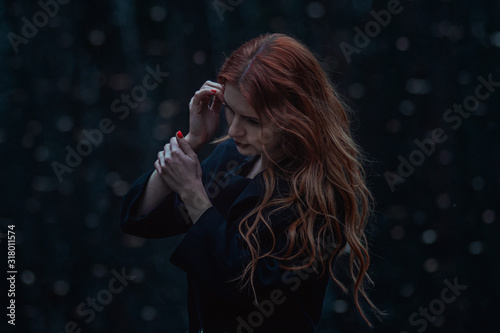 dramatic portrait of beautiful redhead girl in black coat in dark fairytale forest