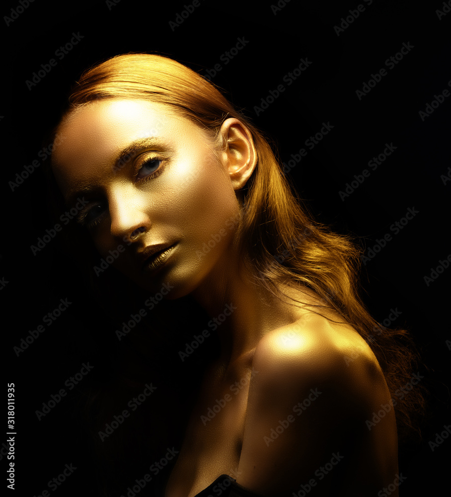 Fototapeta premium Golden woman. Beauty fashion model girl with golden skin, makeup, hair black background. Fashion art portrait shiny