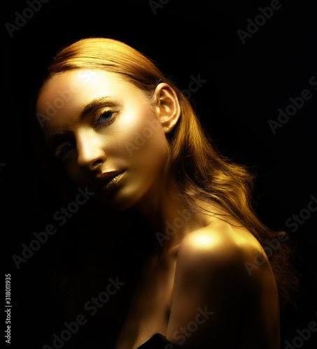 Golden woman. Beauty fashion model girl with golden skin, makeup, hair black background. Fashion art portrait shiny