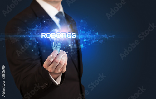 Businessman holding light bulb with ROBOTICS inscription, innovative technology concept
