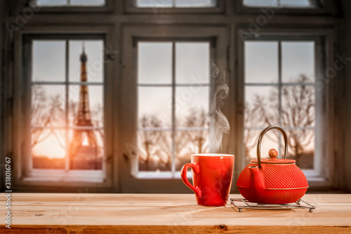 Romantic photo of Valentine's Day red mug on wooden table.Free space for your decoration.Blurred retro old window sill with landscape of Paris city at February.Sun light of orange color and copy space