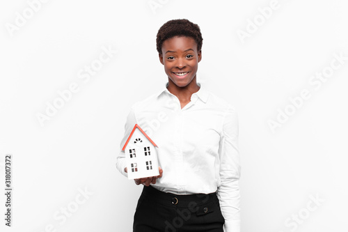 young pretty black womanlooking happy and pleasantly surprised, excited with a fascinated and shocked expression with a house model photo