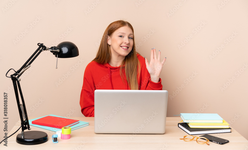 Young student woman in a workplace with a laptop saluting with hand with happy expression Young student woman in a workplace with a laptop saluting with hand with happy expression