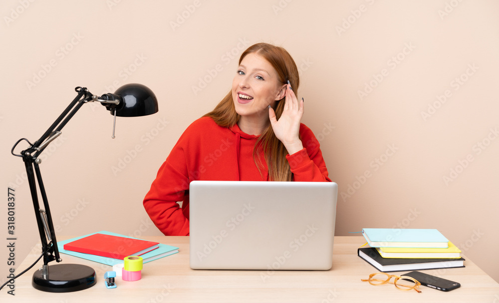 Young student woman in a workplace with a laptop listening to something by putting hand on the ear Young student woman in a workplace with a laptop listening to something by putting hand on the ear