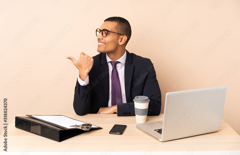 Young business man in his office with a laptop and other documents pointing to the side to present a product Young business man in his office with a laptop and other documents pointing to the side to present a product