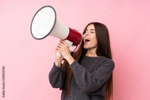 Young woman over isolated pink background shouting through a megaphone