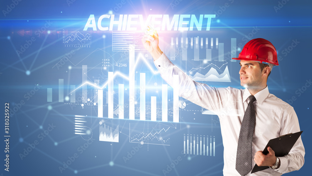 Handsome businessman with helmet drawing ACHIEVEMENT inscription, architecture business plan concept Handsome businessman with helmet drawing ACHIEVEMENT inscription, architecture business plan concept