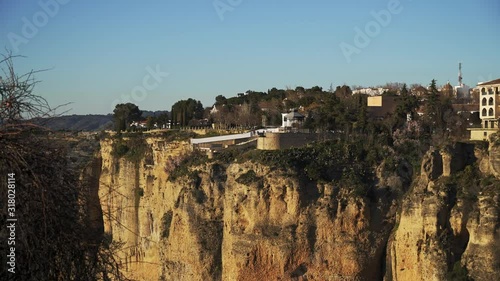 Gimbal pan shot left to right of Ronda city at the cliff under bright blue sky in january. Old stone houses on the cliff in Ronda city under bright blue sky