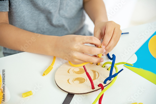 Close up of child hands playing with lace or rope and pasta. development of fine motor skills. Early education  Montessori Method. Cognitive skills 