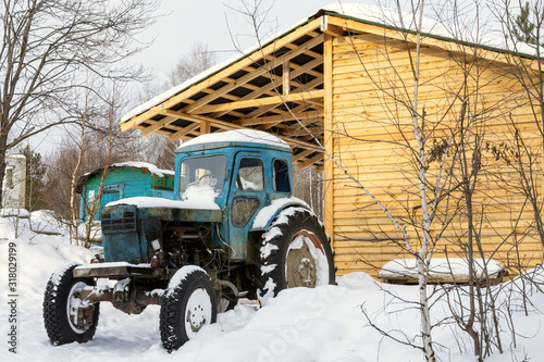 Tractor in the yard of a rural house. Old tractor in the village in winter.