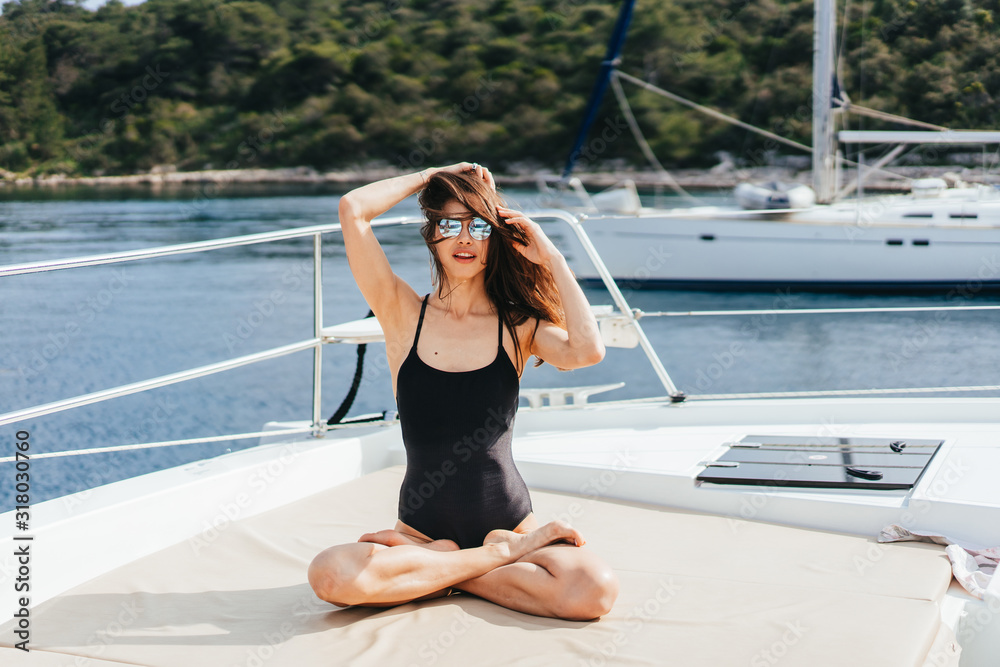 Young healthy and calm woman doing yoga on sailing yacht boat in sea at island background