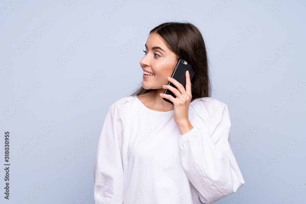 Young woman over isolated blue background keeping a conversation with the mobile phone with someone Young woman over isolated blue background keeping a conversation with the mobile phone with someone