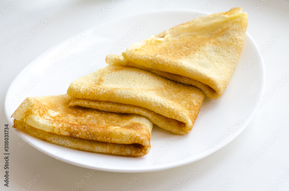 Three pancakes lie on a white plate on a white background. Selective focus. Close up.