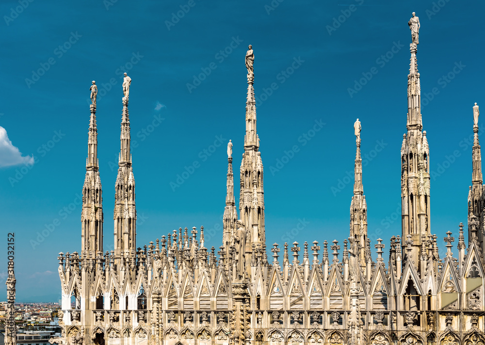 Fototapeta premium Dach katedry w Mediolanie, Włochy. Słynna katedra w Mediolanie lub Duomo di Milano to najważniejszy punkt orientacyjny Mediolanu. Luksusowe gotyckie wieże z posągami na tle błękitnego nieba.